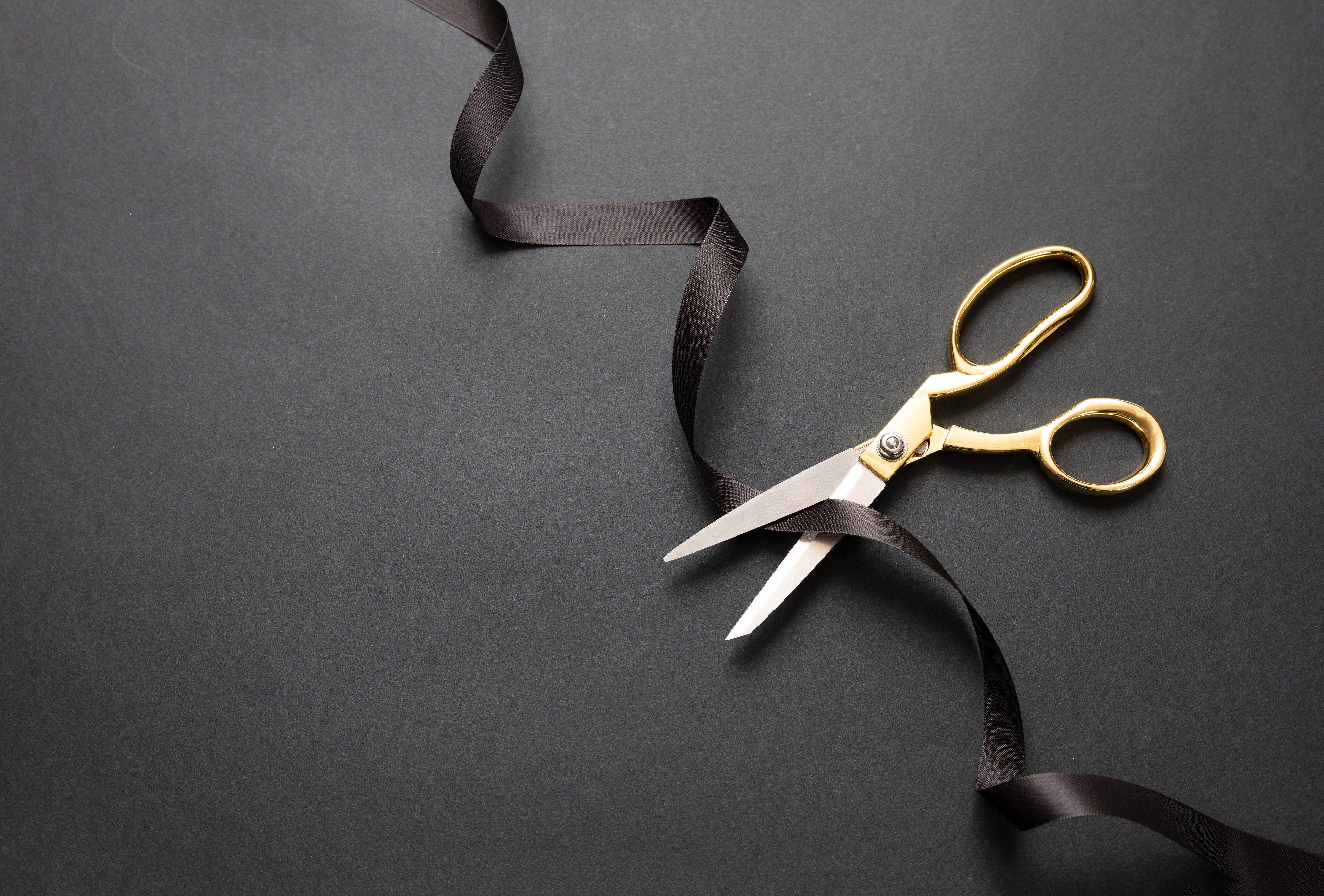 Grand opening. Gold scissors cutting black satin ribbon, black background